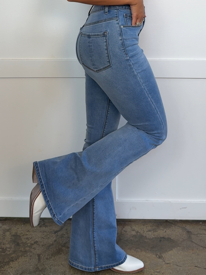 Person wearing blue flared jeans against a white wall.