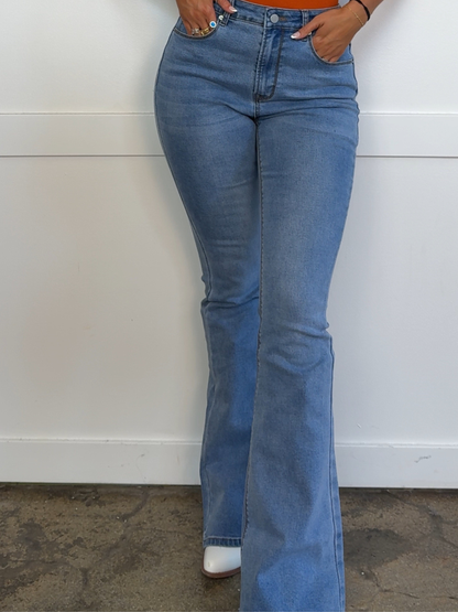 Person wearing blue flared jeans against a white wall.