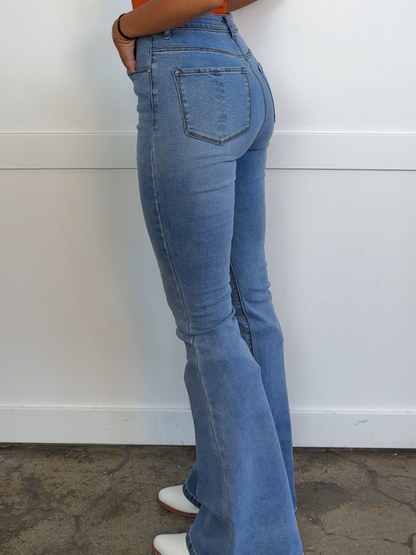 Person wearing blue flared jeans against a white wall.