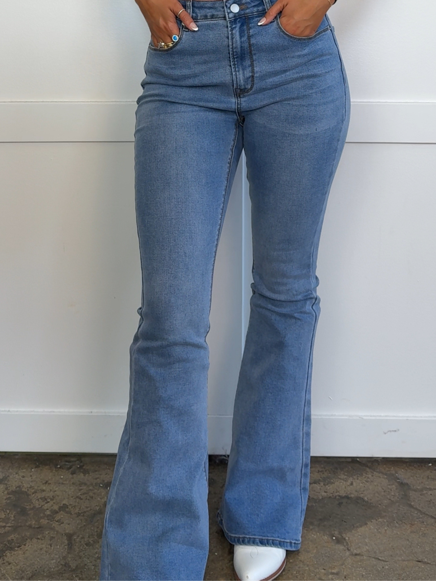 Blue flared jeans worn by a person against a white wall.