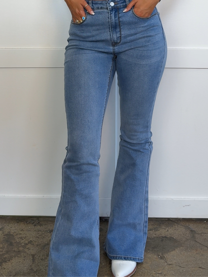 Blue flared jeans worn by a person against a white wall.