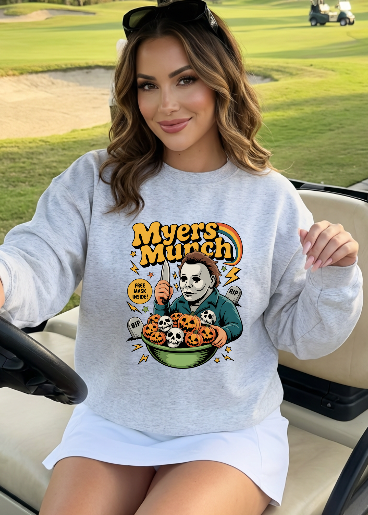 Woman wearing a sweatshirt with a Halloween-themed graphic in a golf cart on a golf course.