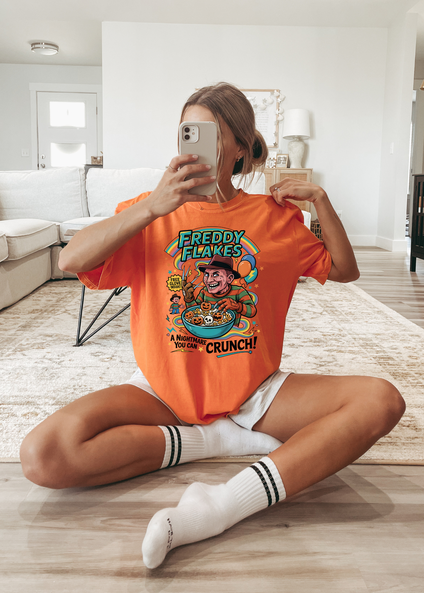 Person wearing an orange t-shirt with a graphic design, sitting on the floor in a modern living room.