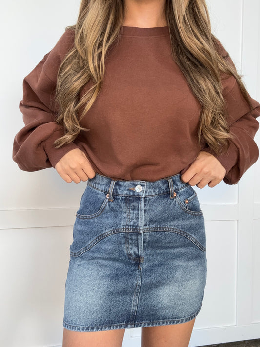 Person wearing a brown shirt and denim shorts against a white background