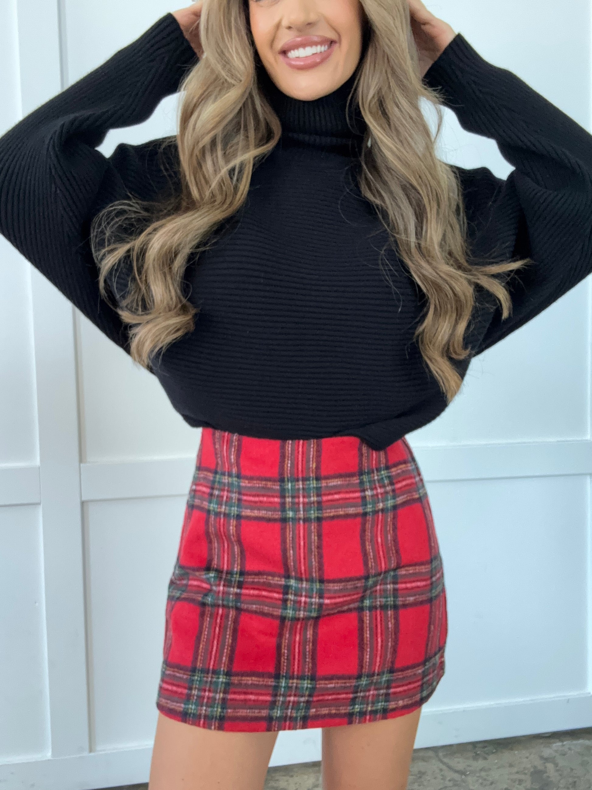 Person wearing a black sweater and red plaid skirt against a white background