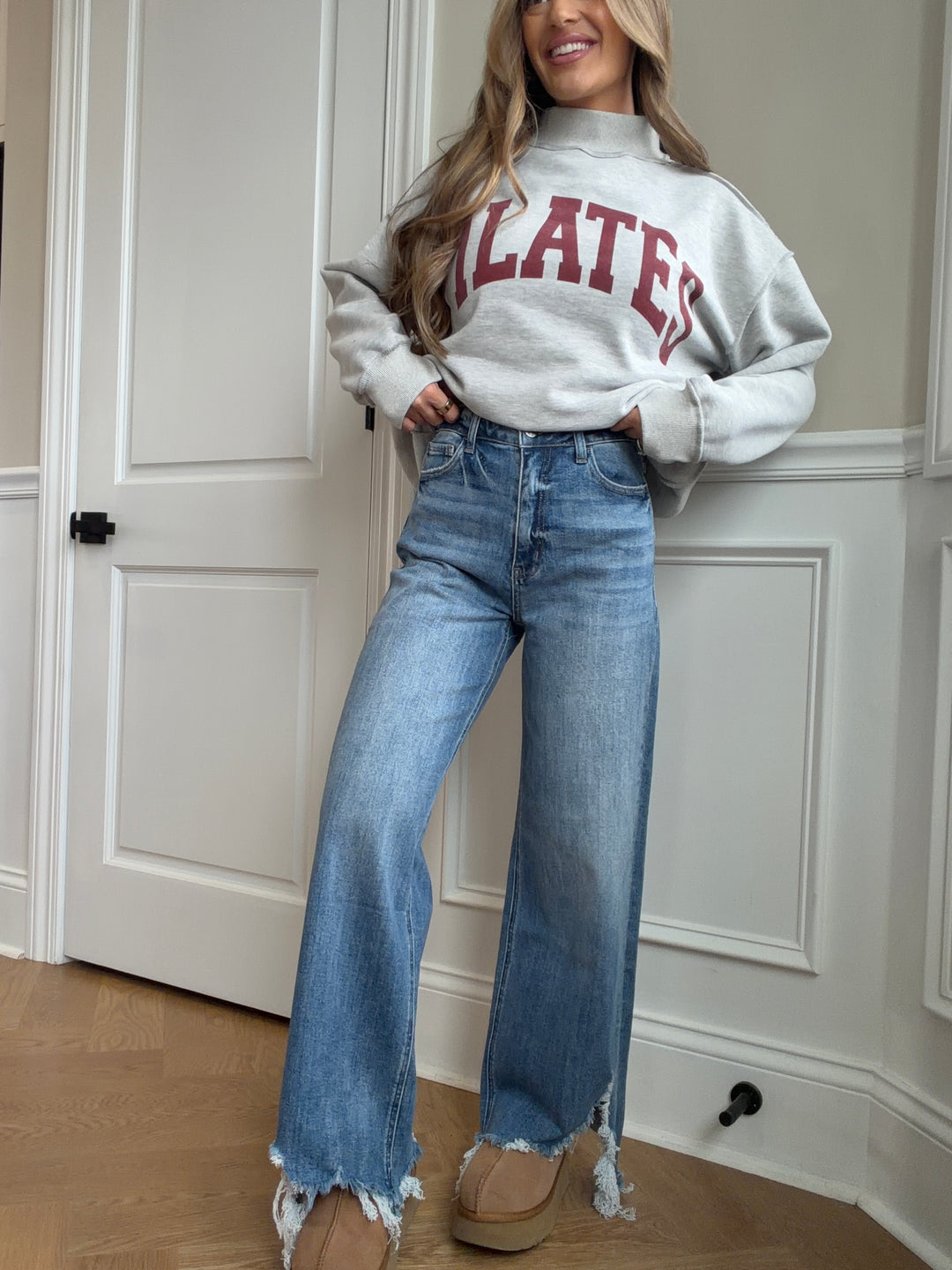Person wearing a gray sweatshirt with 'LATER' text and blue jeans indoors.