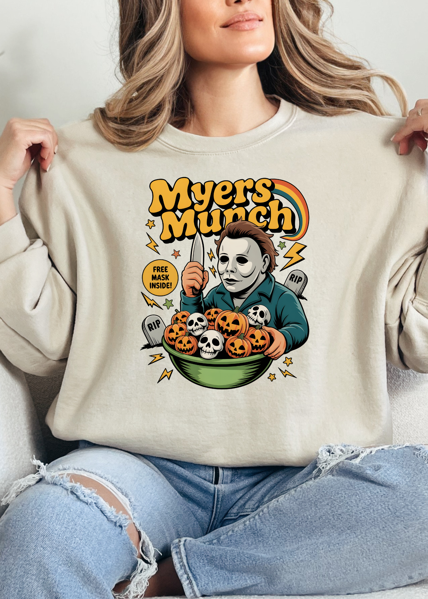 Person wearing a beige sweatshirt with a graphic design featuring a character holding pumpkins and text 'Myers Munch'.