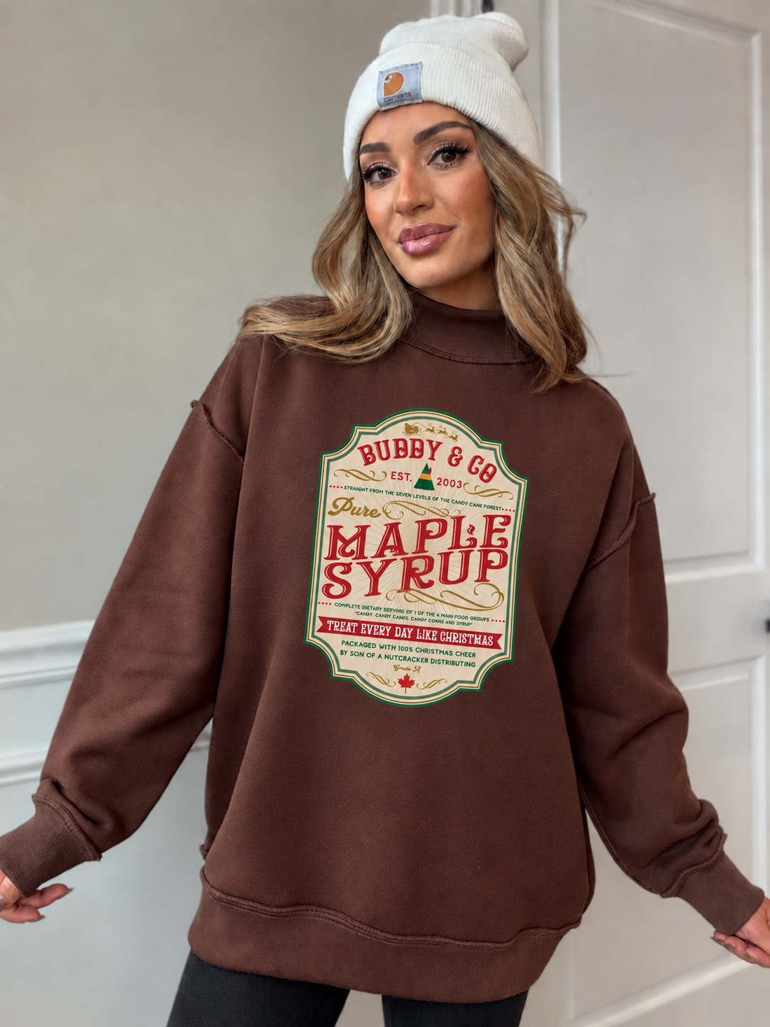 Chelsea in brown oversized mock neck with a smaller centered maple syrup label graphic