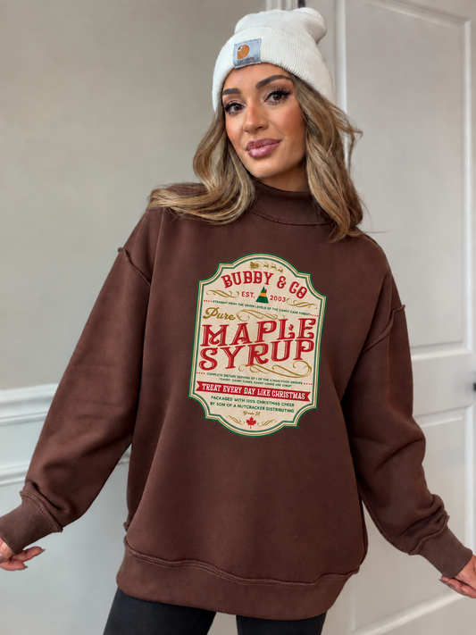 Chelsea in brown oversized mock neck with a smaller centered maple syrup label graphic